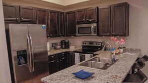 A modern kitchen with a stainless steel refrigerator, microwave, and stove, granite countertops, dark wood cabinets, and a bar area with stools. - Beachside Bliss-Minutes from Beach, Pool, Hot Tub, Near Golf (Miramar Beach)