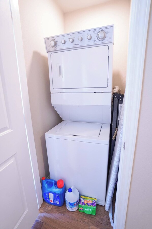 A compact laundry room with a front-loading washer and dryer, a blue detergent container, a bottle of fabric softener, and a box of Gain detergent.