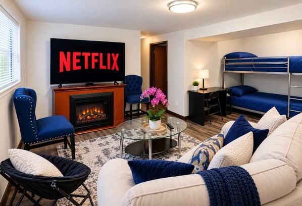 A modern living room with a fireplace, a television displaying 'NETFLIX,' a sofa, a coffee table, and a bunk bed.
