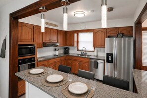 A modern kitchen with wooden cabinets, stainless steel appliances, and a granite countertop. - Midwest Haven- Spacious, Family Home, Near Airport (Kansas City)