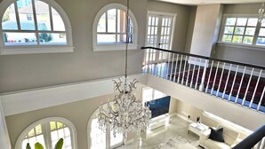Un intérieur spacieux avec un plafond haut, un lustre, un grand téléviseur et un balcon.