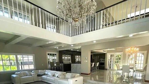 Un vaste espace de vie comprenant un grand canapé d’angle blanc, un lustre et un balcon doté d’une balustrade.