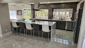 Une cuisine moderne dotée d’un grand îlot central, de tabourets de bar, d’appareils électroménagers en acier inoxydable et de grandes fenêtres.