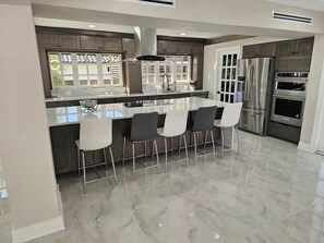 Cozinha moderna com ilha central, eletrodomésticos de aço inoxidável e espaço de bar com banquetas.
