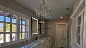 Une salle de bain avec une grande fenêtre, un lustre et un miroir.