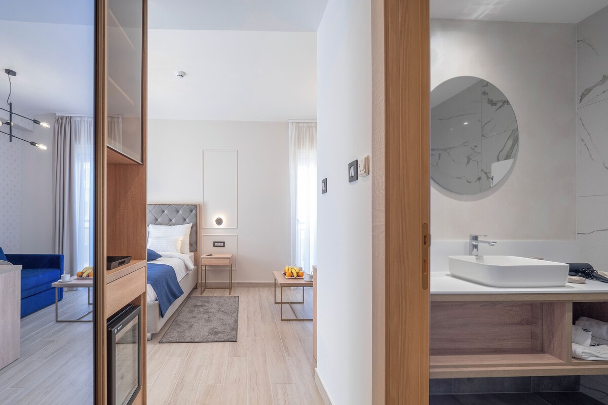 A modern hotel room with a bed, bedside table, and a bathroom with a sink and mirror.