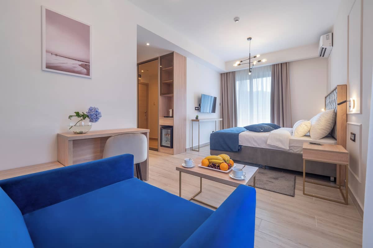 Una habitación de hotel moderna con una cama, un escritorio, un sofá azul, una mesita con fruta y un televisor.
