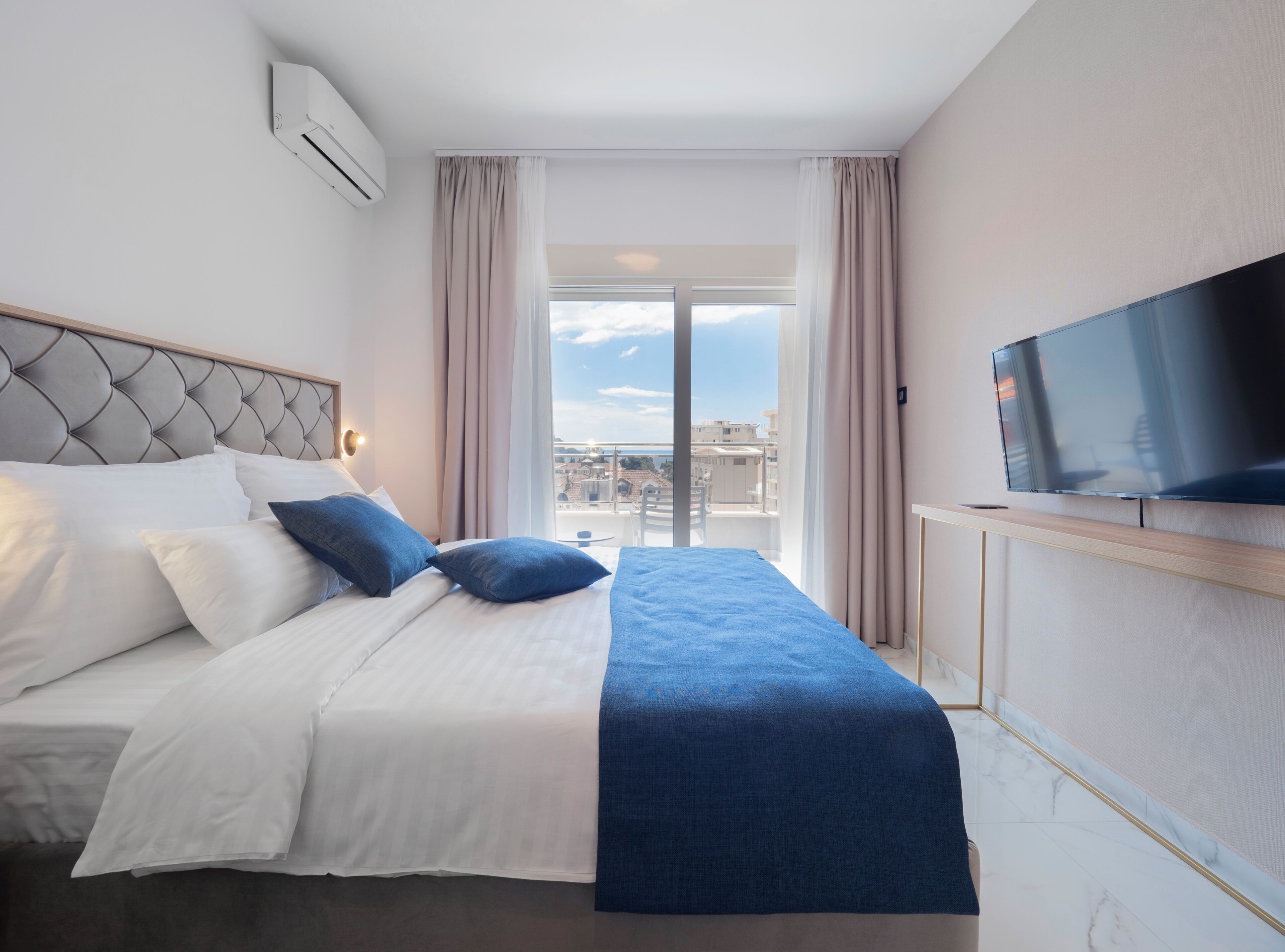 Una habitación de hotel con cama, televisión, ventana y aire acondicionado.