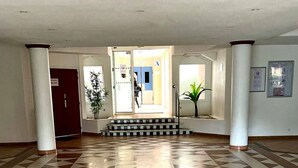 A spacious lobby with a geometric patterned floor, a staircase leading to an upper level, and a door marked with a wheelchair symbol. - Residence Domaine de Valescure Saint-Raphaël (Saint-Raphaël)