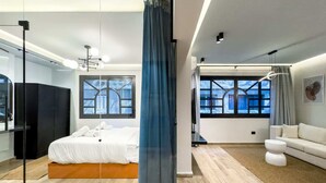 A modern bedroom with a bed, a large window, a sofa, and a mirror.