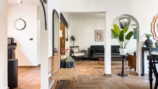A modern living room with a herringbone floor, a large mirror, a green sofa, a coffee table, and a potted plant.
