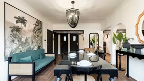 A dining area with a black table set for four, a sofa with cushions, and a large painting of tropical foliage on the wall.