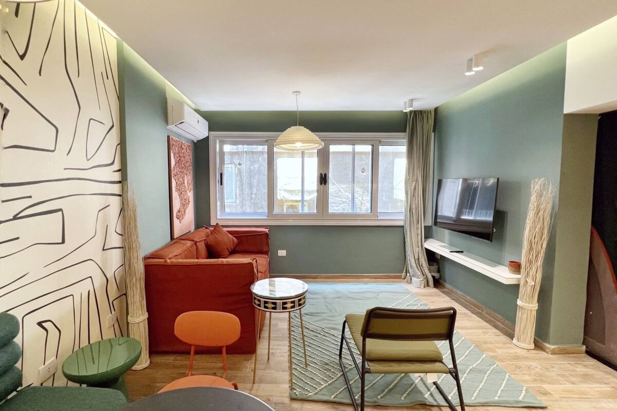Ein modernes Wohnzimmer mit einer Couch, Sesseln, einem Fernseher und einem großen Fenster.