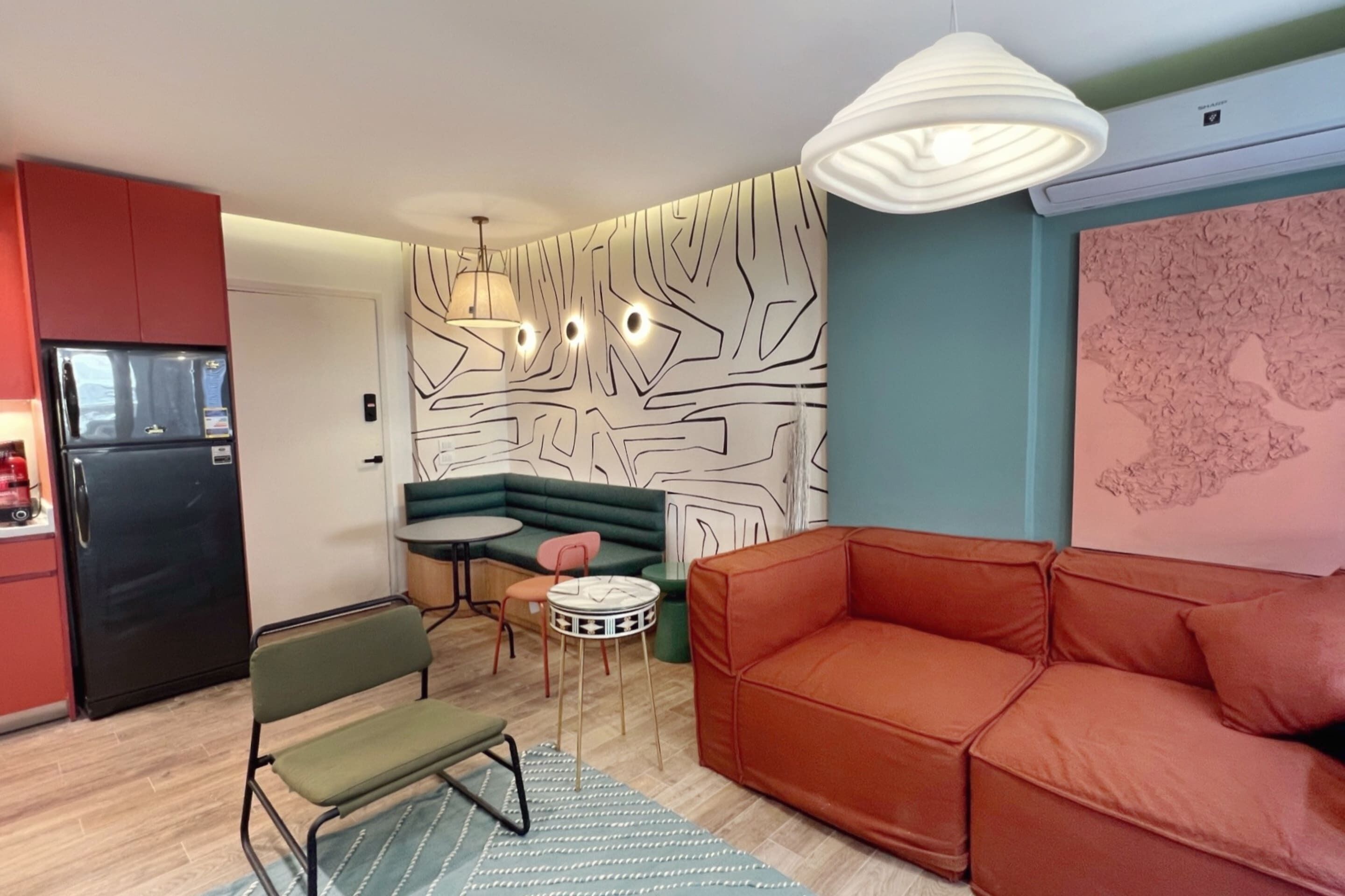 A compact living space with a kitchenette, a green sofa, a red sofa, and a patterned wall.