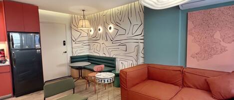 A compact living space with a kitchenette, a green sofa, a red sofa, and a patterned wall.