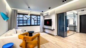 A modern living room with a sofa, a coffee table, a TV, and a glass door leading to a bathroom. - Xuru Stays I Heliopolis 1 - 5 Min to Airport (Cairo)