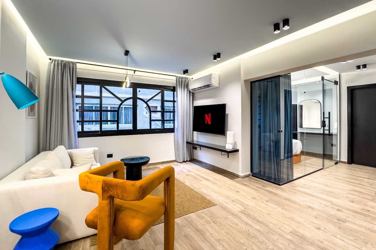A modern living room with a sofa, a coffee table, a TV, and a glass door leading to a bathroom.