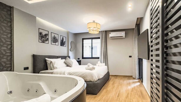 A modern hotel room with a large bed, a separate sitting area, a bathtub, and a window with curtains. - Xuru Stays I Heliopolis 1 - 5 Min to Airport (Cairo)
