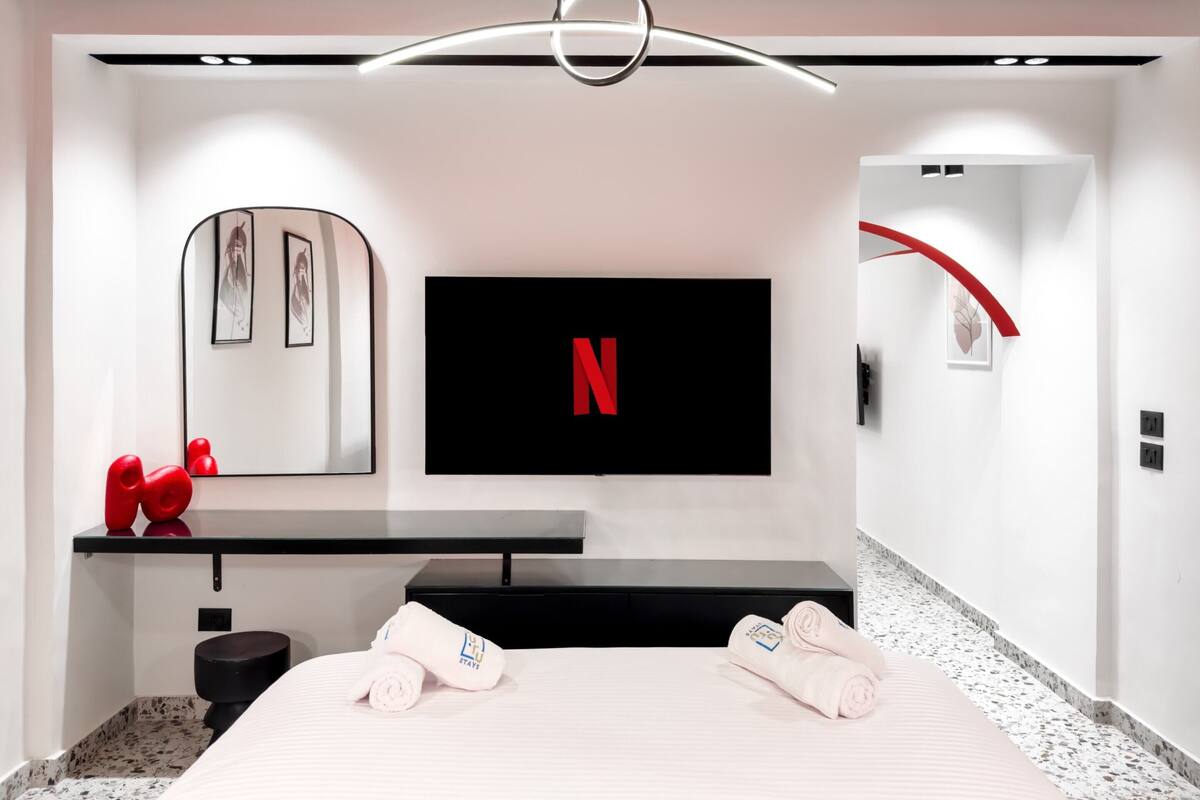 A modern hotel room with a flat-screen TV mounted on the wall, a black console table, and a bed with neatly folded towels.