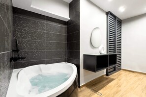 Un baño moderno con una bañera independiente, paredes de azulejos negros, suelo de madera y un estante negro con un objeto blanco encima.