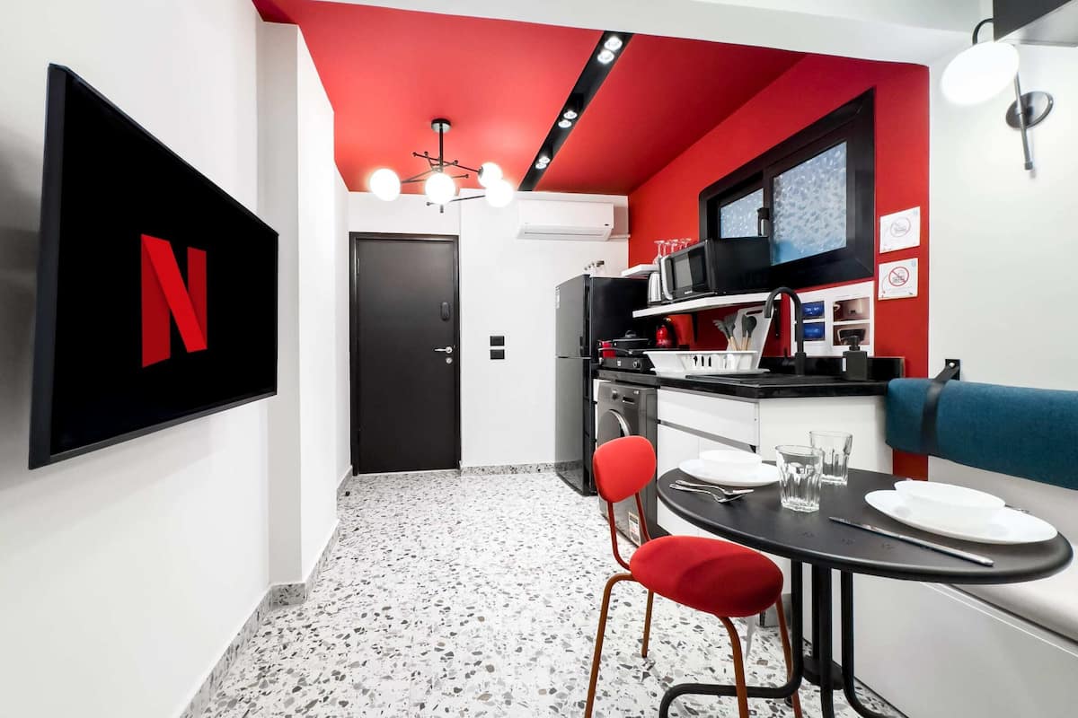 A compact kitchen with a microwave, sink, and red chairs. A large Netflix logo is on the wall.