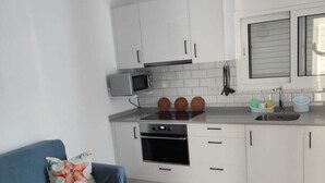 Une cuisine moderne avec des meubles blancs, un four à micro-ondes, un four et un évier. On y trouve un canapé bleu avec un coussin en forme d’étoile de mer.