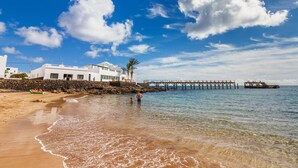 Une plage avec un bâtiment blanc, une jetée et un ciel bleu dégagé.