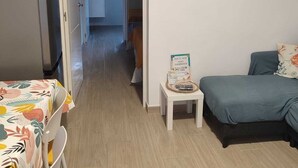 Une pièce comprenant un lit, une petite table avec un panneau, un réfrigérateur et une porte donnant sur une autre pièce.