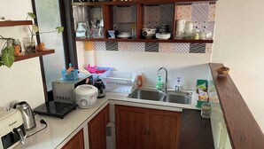 A compact kitchen with wooden cabinets, a built-in sink, and a countertop with various appliances and utensils. - Blue Beach Village (Da Nang)