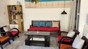 A living room with a sofa, chairs, a coffee table, a bookshelf, and a beach-themed painting on the wall. - Blue Beach Village (Da Nang)