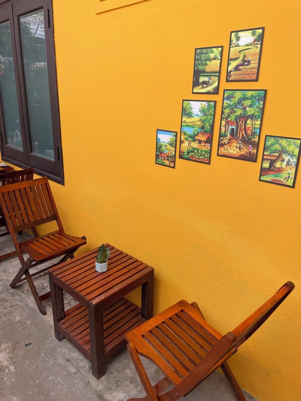 A room with wooden furniture, a small table with a plant, and a yellow wall with framed pictures.
