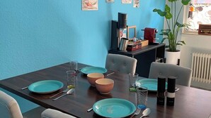 Ein Essbereich mit einem dunklen Holztisch, gedecktem für vier Personen, hellgrauen Stühlen und einer blauen Wand mit Vintage-Dekorationen im Diner-Stil.
