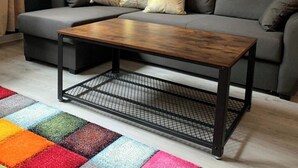 Ein Wohnzimmer mit grauem Sofa, einem Holztisch und einem bunten Teppich.
