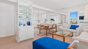 A modern living room with a dining area, white cabinetry, and a large window with a view. - The Hideaway at Ocean Isle Beach (Ocean Isle Beach)