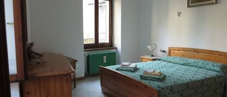 A bedroom with a wooden bed, a nightstand, a chair, a radiator, and a window.