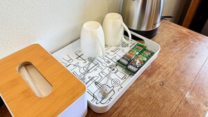 Un tavolo di legno con un vassoio bianco che contiene due tazze bianche, un bollitore in acciaio inossidabile e un vassoio con cialde per caffè.