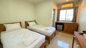 Una camera d'albergo con due letti singoli, una scrivania, un frigorifero e una finestra con tende.