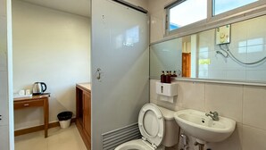 Un bagno moderno con il water, un lavandino e una doccia. Si nota un mobiletto in legno e un bollitore su un tavolo.