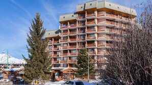 A multi-story hotel with balconies, a ski lift in the background, and a snow-covered ground. - Lovely apartment for 6 guests with WIFI, TV and balcony (Les Deux Alpes)
