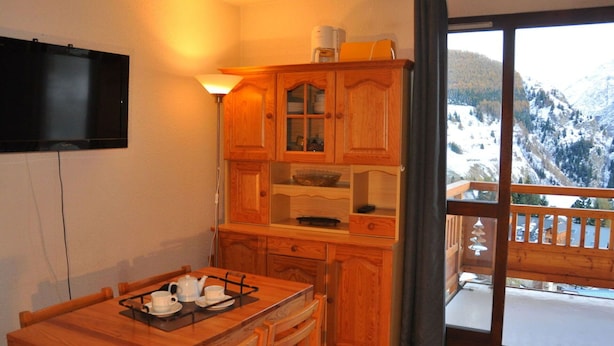 Eine gemütliche Küche mit Holzschränken, einem Esstisch mit Tee-Service und Blick auf verschneite Berge vom Balkon aus.