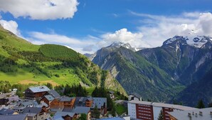 Ein Bergdorf mit traditionellen Holzhäusern, einem Skigebiet und Blick auf verschneite Berggipfel.