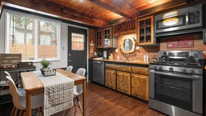A cozy kitchen with wooden cabinets, a stainless steel stove, and a dining area with a table and chairs. - Moonridge Manor Cozy Retreat with Hottub (Big Bear Lake)