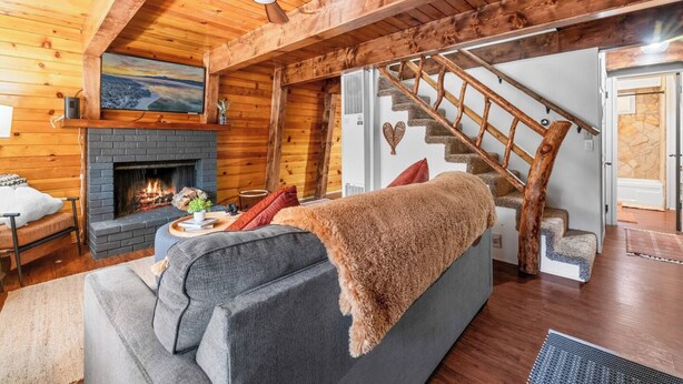 A cozy living room with a fireplace, a sofa, a staircase, and a wooden ceiling. - Moonridge Manor Cozy Retreat with Hottub (Big Bear Lake)