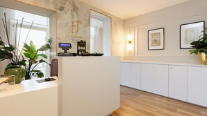 A reception area with a marble wall, a reception desk, a plant, framed certificates, and a wooden floor.