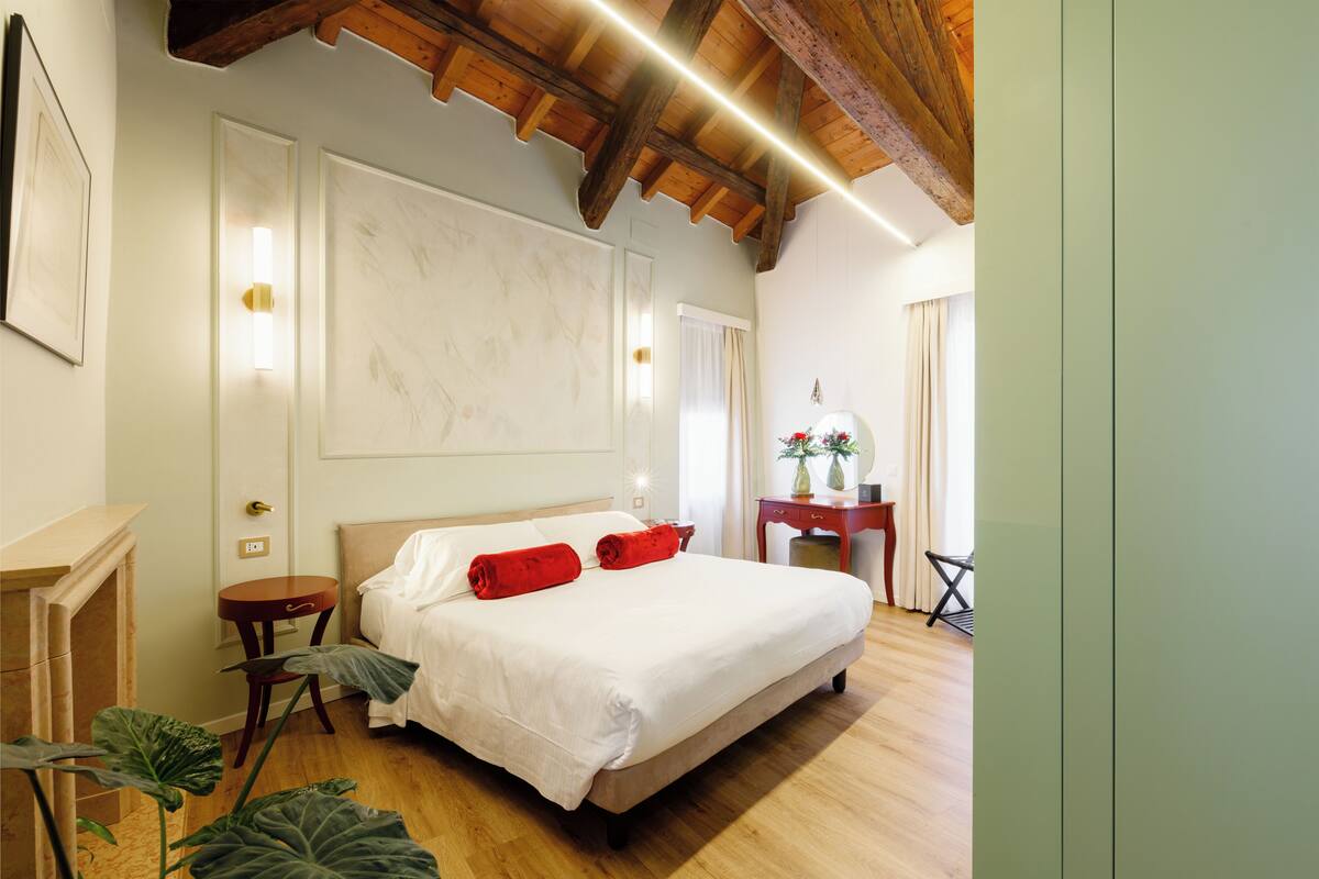 Une chambre avec un grand lit, un plancher en bois et un plafond avec des poutres apparentes.