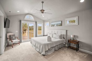 A bedroom with a bed, a chair, a bedside table, a ceiling fan, and a view through a glass door.