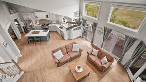 A modern kitchen with white cabinets, a central island, and a dining area with a brown leather sofa and a coffee table.