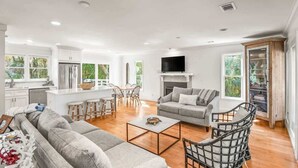 A modern living room with a sofa, coffee table, and chairs, a kitchen area with a refrigerator, and a fireplace. - 374 Perch Drive (Fripp Island)