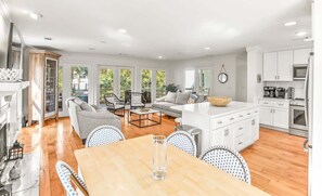 Amplia sala de estar con una mesa de comedor, sofás y una cocina con armarios y electrodomésticos blancos.