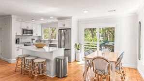 A modern kitchen with white cabinetry, a stainless steel refrigerator, and a dining area with wicker chairs. - 374 Perch Drive (Fripp Island)